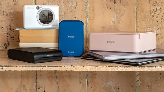 Canon Zoemini and SELPHY range printers placed with some books on a wooden shelf.