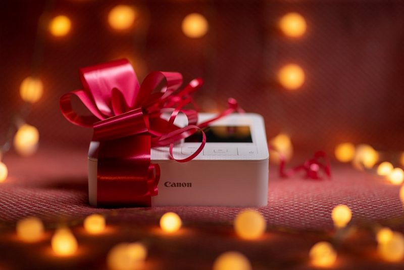 A Canon SELPHY printer with a red bow wrapped around it and twinkly fairy lights all around it. 