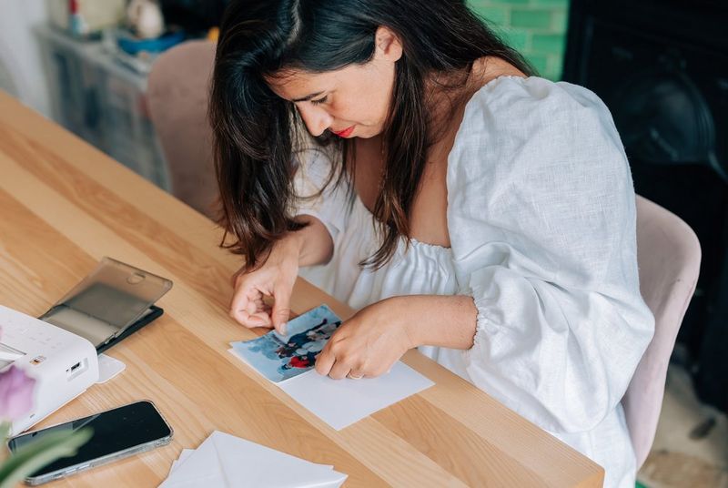 A woman at a table sticking a family photo onto a piece of card.