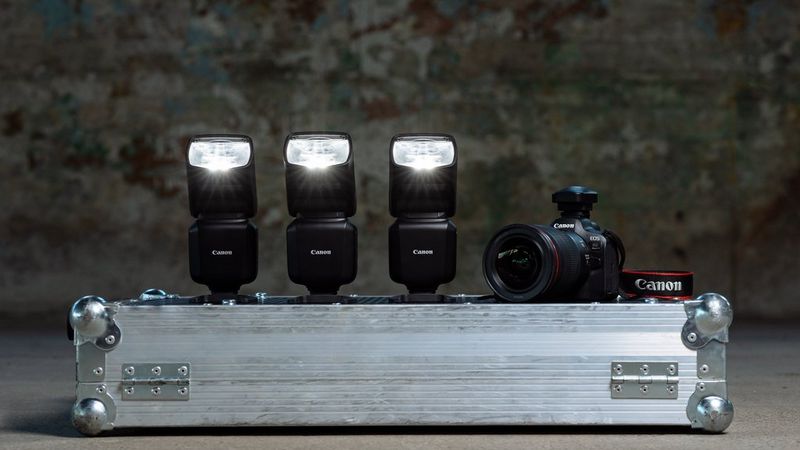 Three Canon Speedlite EL-5s and a Canon EOS R6 Mark II lined up in a row on top of a silver flight case. 