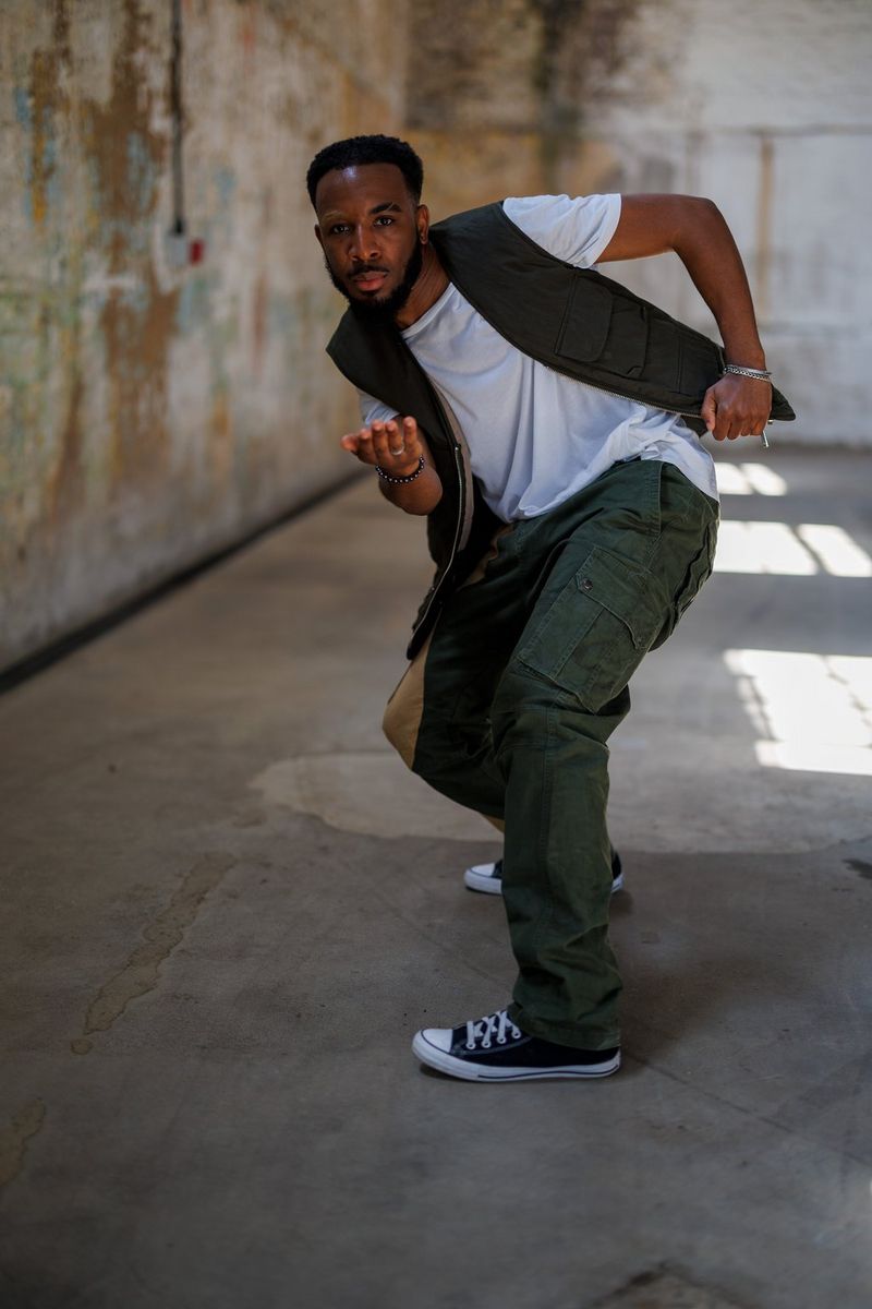 A dancer in cargo pants and trainers in a dimly lit warehouse photographed without a flash by David Newton.