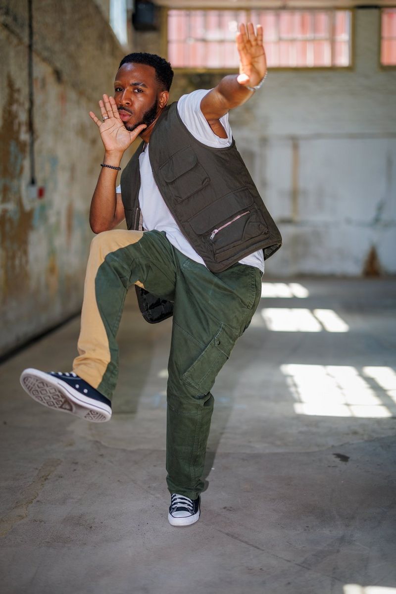 A dancer in cargo pants and trainers photographed by David Newton in a dimly lit warehouse using a single Speedlite EL-5.