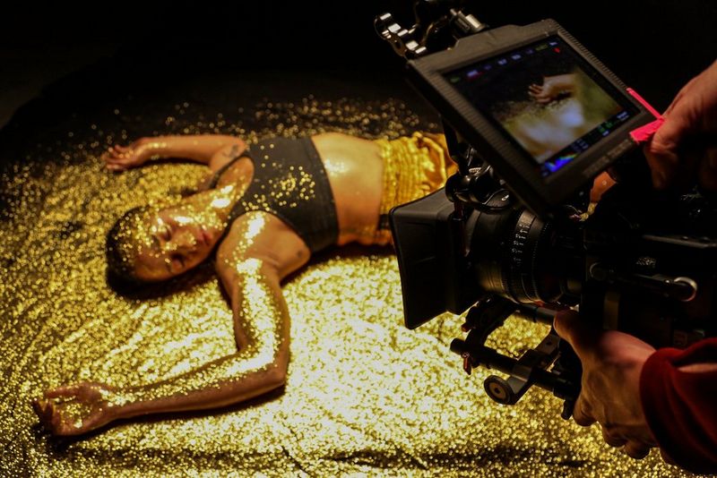 A female athlete is filmed lying in a pool of golden glitter using Canon Sumire Prime lenses.