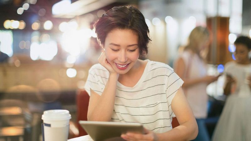 An image of a woman smiling at her tablet