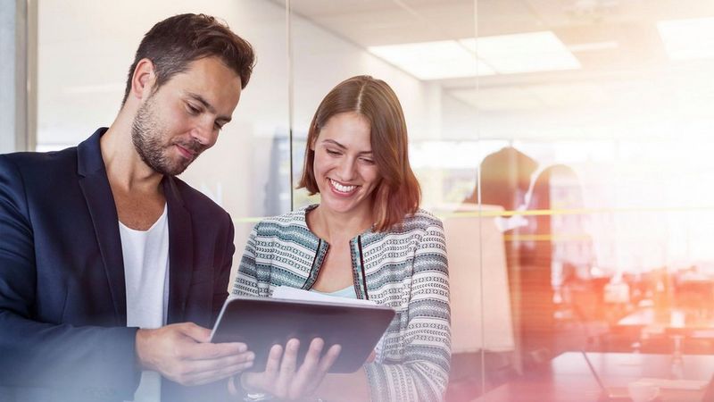 An image of two adults smiling at a tablet 
