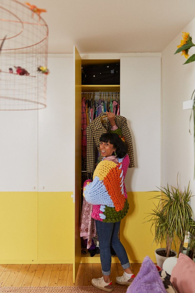 A woman in a brightly coloured jumper getting a jacket out of a wardrobe.