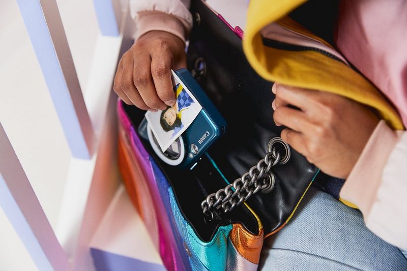 A person putting the blue Canon Zoemini S2 into a handbag.