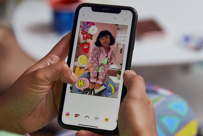 Hands holding a phone while adding stickers to an image in the Canon Mini PRINT app.