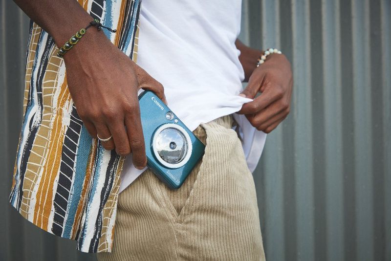 A man wearing beige trousers and a colourful shirt slides a Canon Zoemini S2 photo printer into his pocket. 