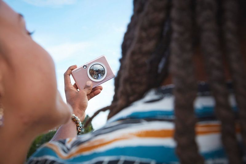 A man and woman taking a selfie with a pink Canon Zoemini S2. The camera is in focus but the couple are blurred. 