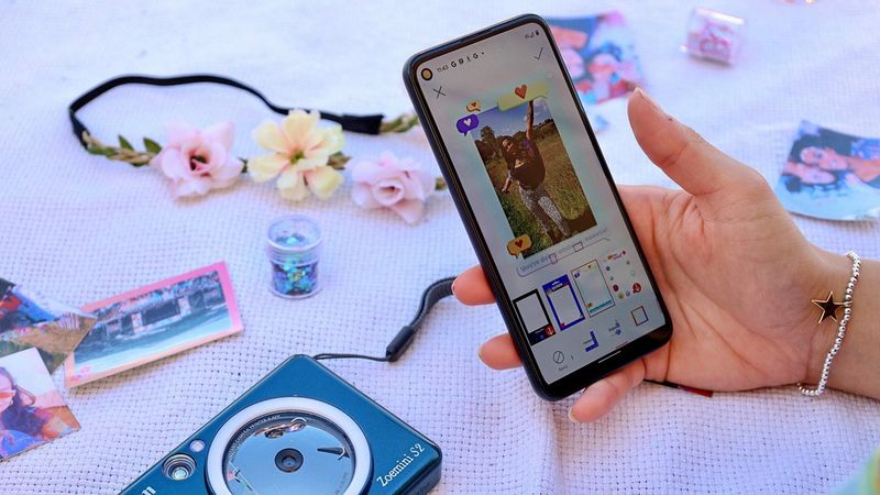 A hand holding smartphone with Mini Print App on the screen showing a photo of a young woman with different app effects applied. Canon Zoemini S2 is visible in the background.