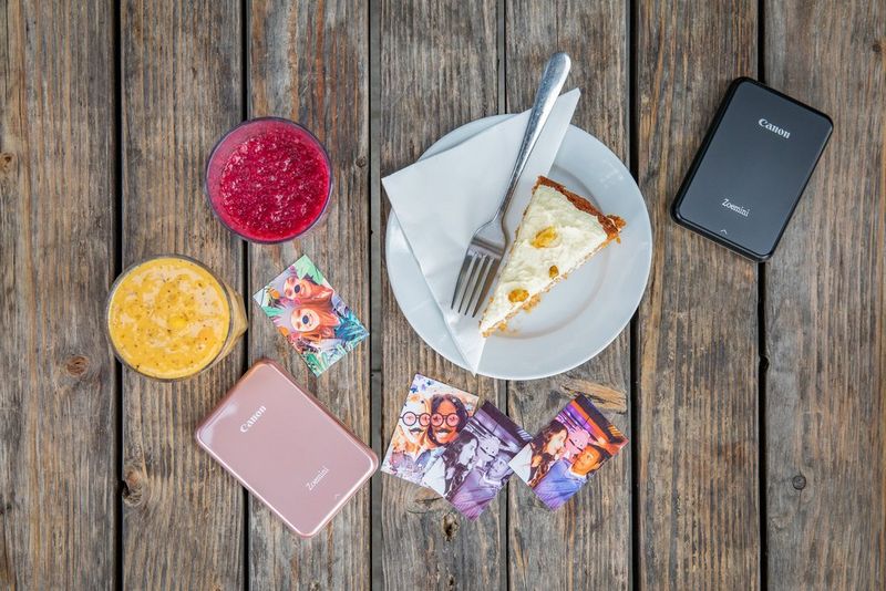Two Canon Zoemini printers on a table top with a plate of cake, and some drinks. 