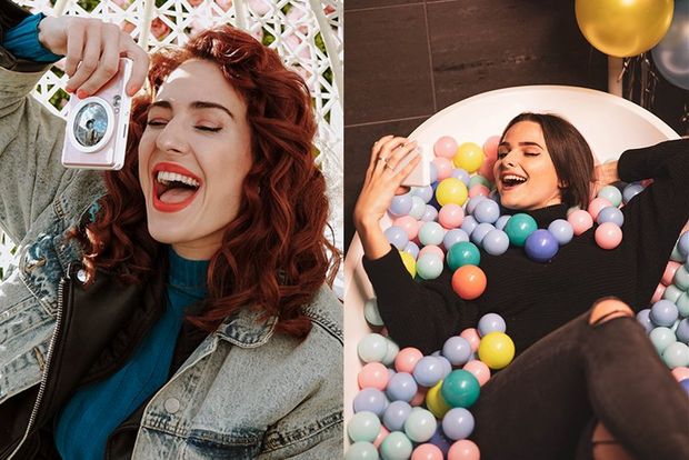 2 young women - one taking a photo with Canon Zoemini S, one taking a selfie in a bathtub filled with colourful balls.