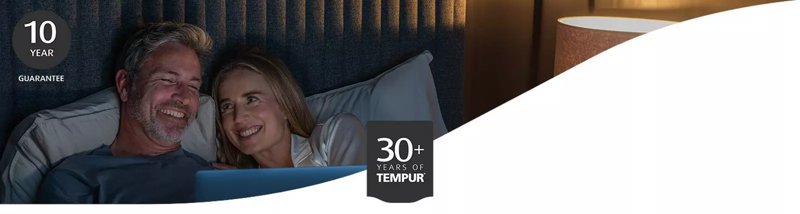 A couple in bed smiling with icons of 30 years of Tempur and 10 year guarantee