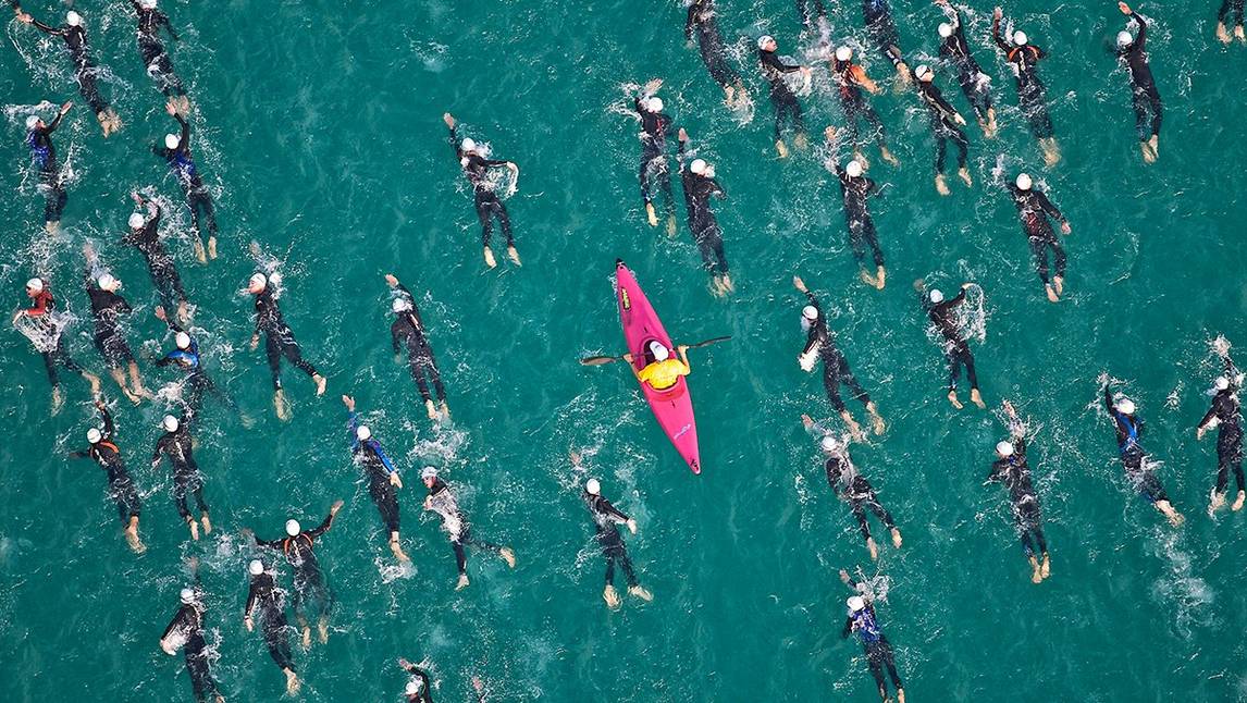Sekelompok orang berenang di laut dengan kayak merah muda di tengahnya