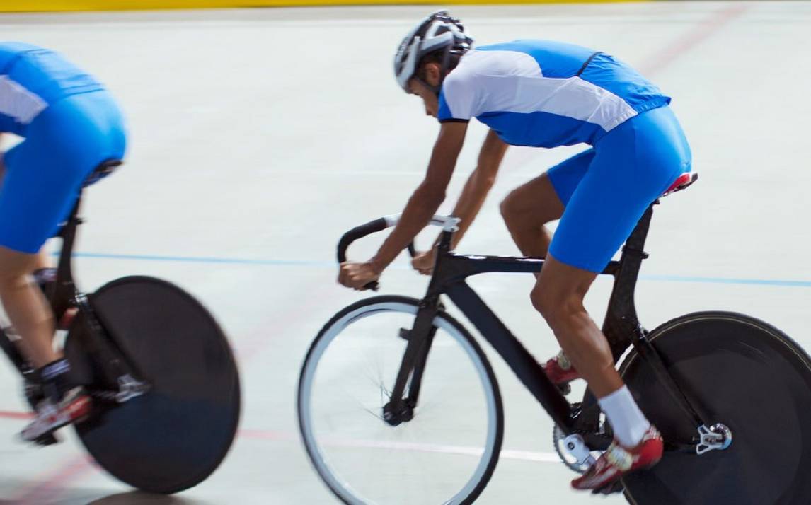 Two professional track cyclists in blue and white kit ride wheel-to-wheel as they compete in the velodrome.