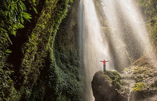 Man with his arms outstretched stood on a rock underneath a waterfall