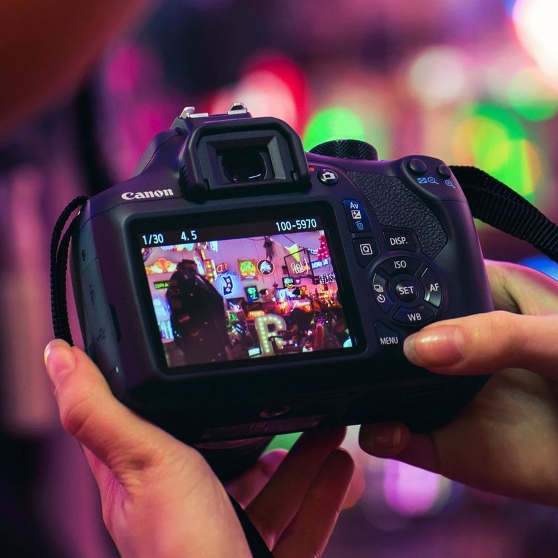 Canon EOS 1300D Black + EF-S 18-55mm III Lens + Shoulder Bag + SD Card Camera Holding With Two Hands With Back View