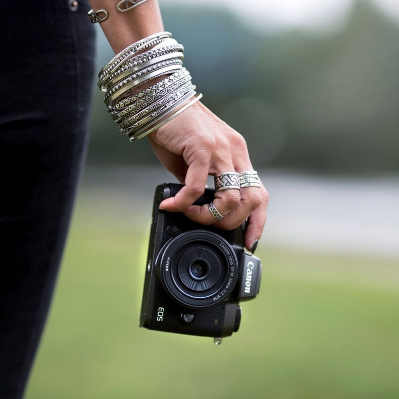 Canon EOS M5 + EF-M 18-150mm f/3.5-6.3 IS STM 0 Main accessoirisée tenant l'appareil photo