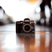 Canon EOS M5 + EF-M 18-150mm f/3.5-6.3 IS STM Lens Camera on the floor with a blurry background