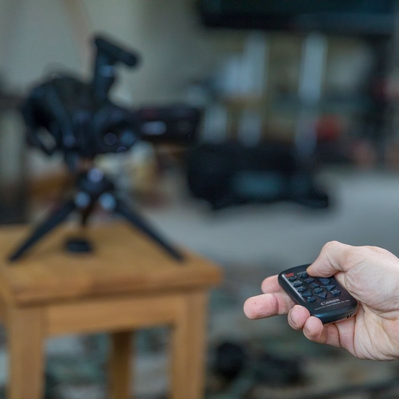 Canon LEGRIA GX10 Remote Control in Hand with Blurry Camera in the Background