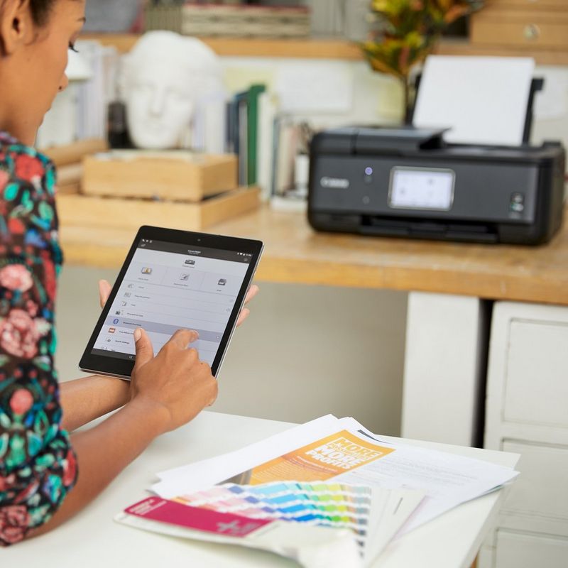 Canon PIXMA TR8550 Auf einem Tisch vor einer Person, die ein Smartphone nutzt