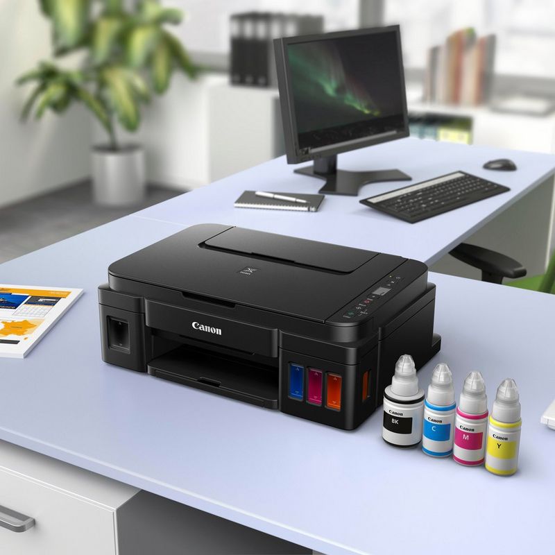 Impresora Canon PIXMA G2510 Sobre una mesa de oficina junto con las botellas de tinta