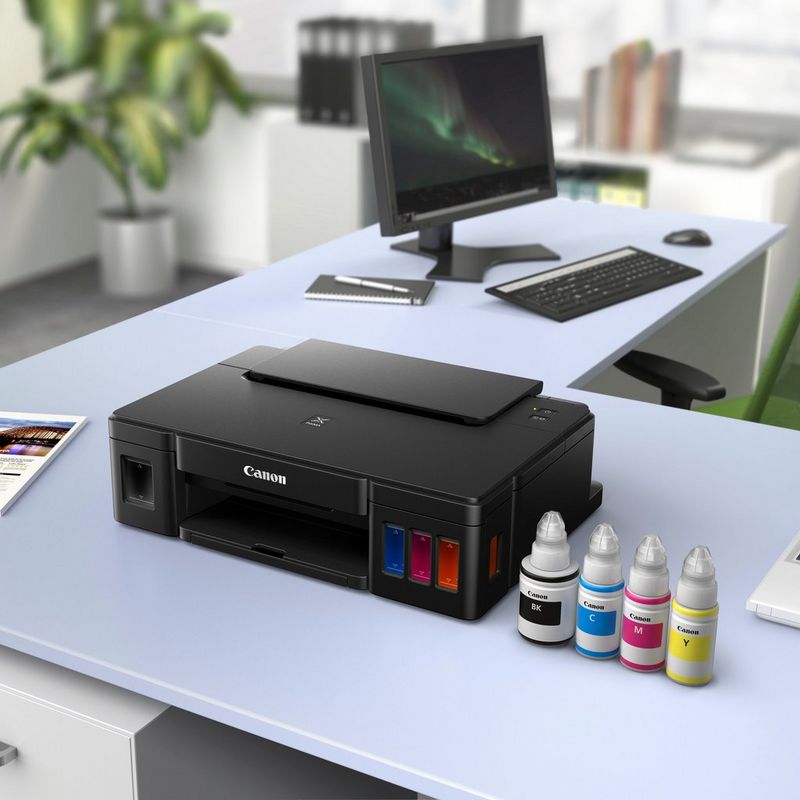 Canon PIXMA G1510 Refillable MegaTank Printer Kept On A Office Table Beside a Monitor and Along with the Ink Bottles