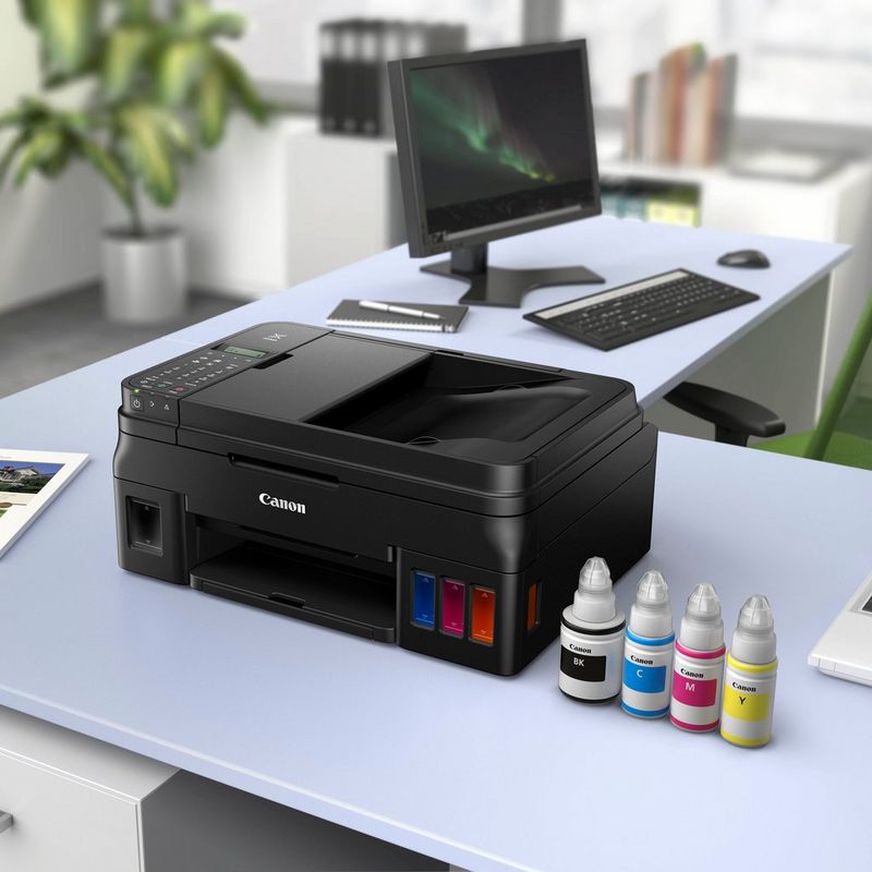 Canon PIXMA G4510 Refillable MegaTank Printer Kept On A Office Table Beside a Monitor and Along with the Ink Bottles