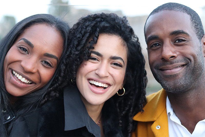 A close-cropped portrait of three smiling people with the background blurred behind them.