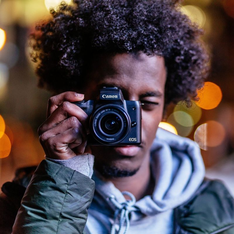 Canon EOS M50 Noir + objectif EF-M 15-45mm STM Noir 0 Un homme tenant l'appareil photo près de son visage
