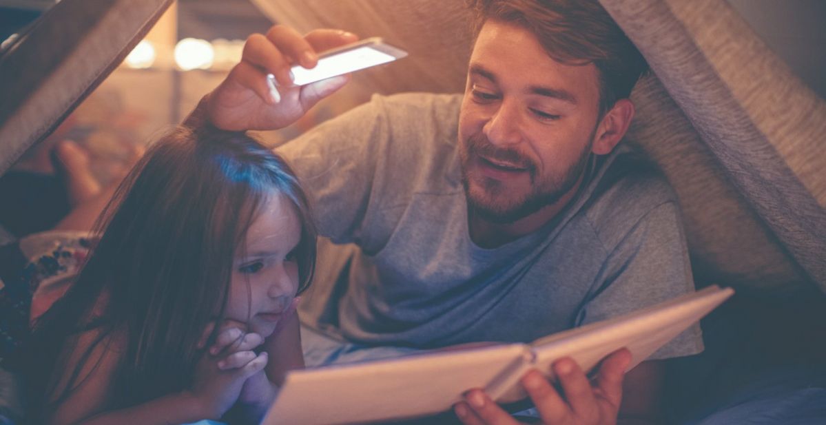 A man and a child reading a hardback book by the light of a smartphone