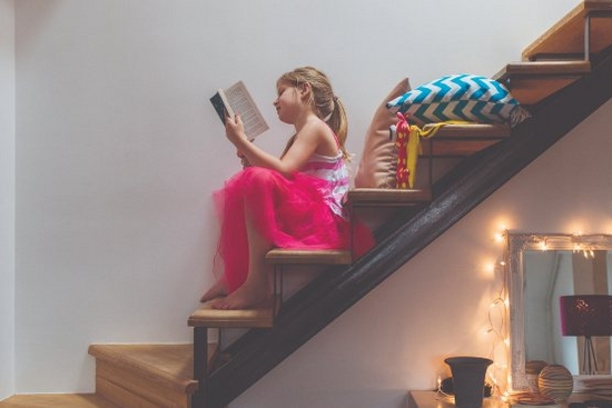 A young girl sitting reading a paperback book on some stairs