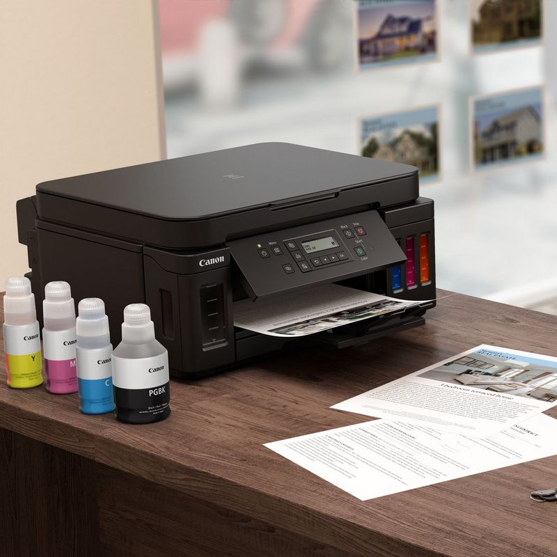 Canon PIXMA G6050: impresora MegaTank 3 en 1 con depósitos de tinta rellenable Sobre una mesa con la bandeja de papel abierta junto a las botellas de tinta