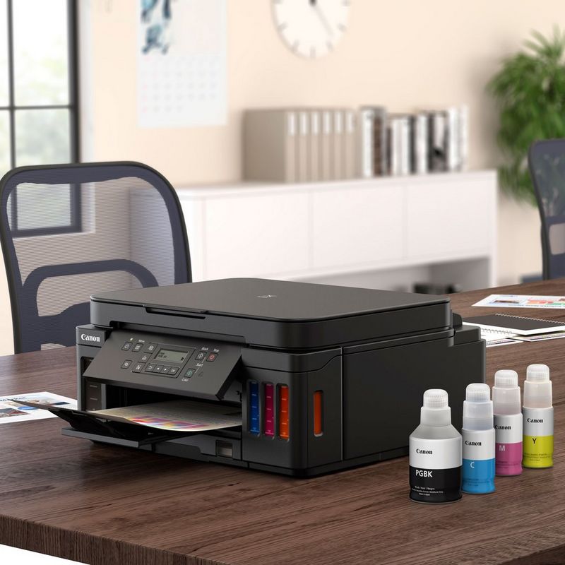 Canon PIXMA G6050: impresora MegaTank 3 en 1 con depósitos de tinta rellenable Sobre una mesa con la bandeja de papel abierta junto a las botellas de tinta