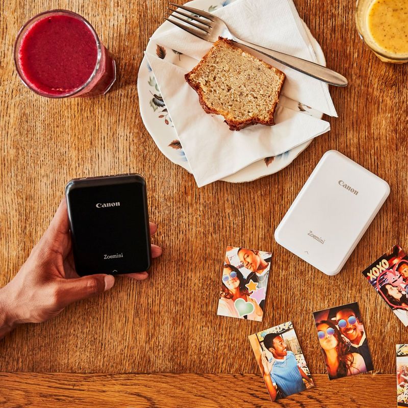 Impresora fotográfica portátil Canon Zoemini, blanco Una mano sostiene una impresora sobre un escritorio
