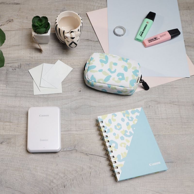 Impressora Fotográfica a Cores Portátil Canon Zoemini, Branco + Diário + Bolsa Impressora posicionada numa secretária ao lado de uma chávena