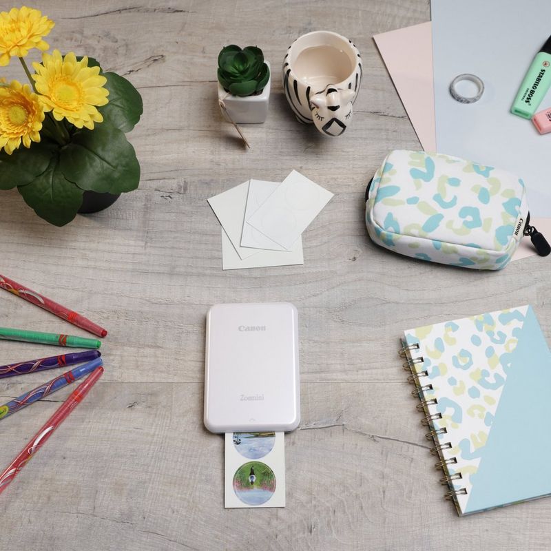 Impressora Fotográfica a Cores Portátil Canon Zoemini, Branco + Diário + Bolsa Impressora posicionada numa secretária ao lado de umas canetas