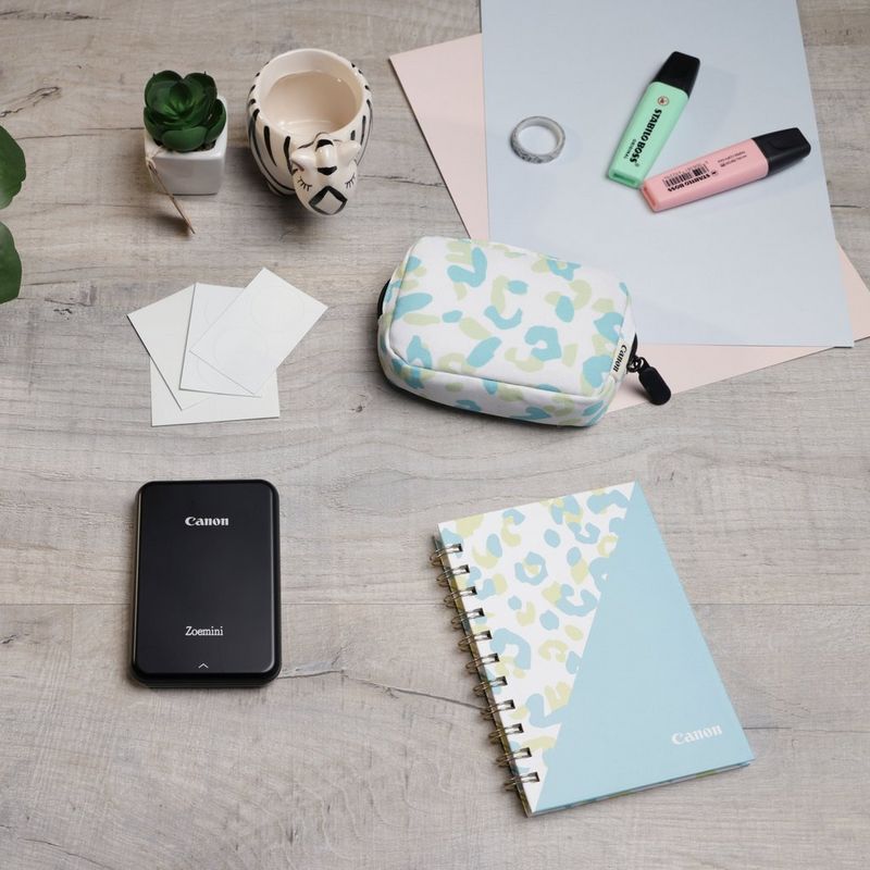Canon Zoemini bärbar färgfotoskrivare, svart + dagbok + väska  En skrivare placerad på ett skrivbord med en kopp