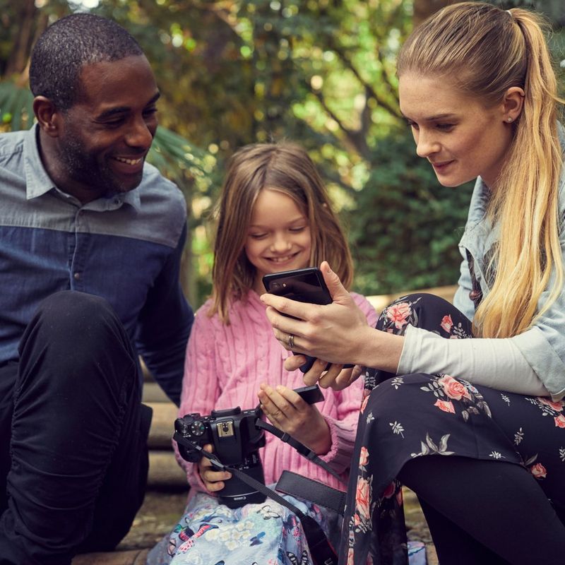 Canon EOS 250D Gehäuse, Schwarz Familie, die ein Foto auf einem Mobiltelefon ansieht