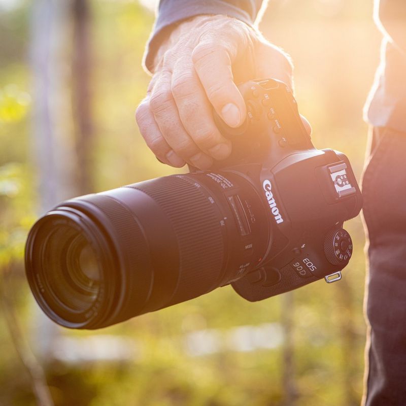 Canon EOS 90D + EF-S 18-135mm IS USM Objektiv + Rucksack + SD Karte + Ersatzakku Mann, der eine Kamera im Freien hält