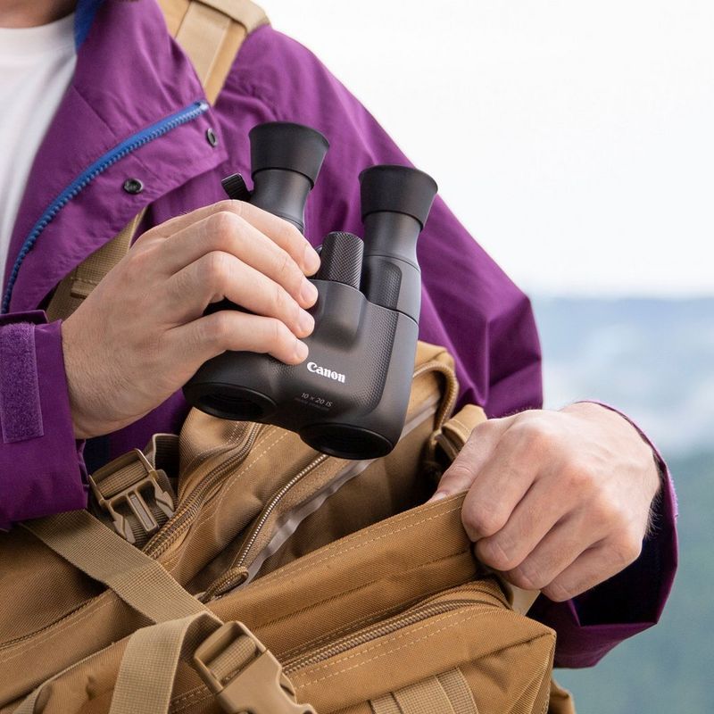 Jumelles Canon 10x20 IS Homme tenant des jumelles, sur le point de les ranger dans un sac en bandoulière