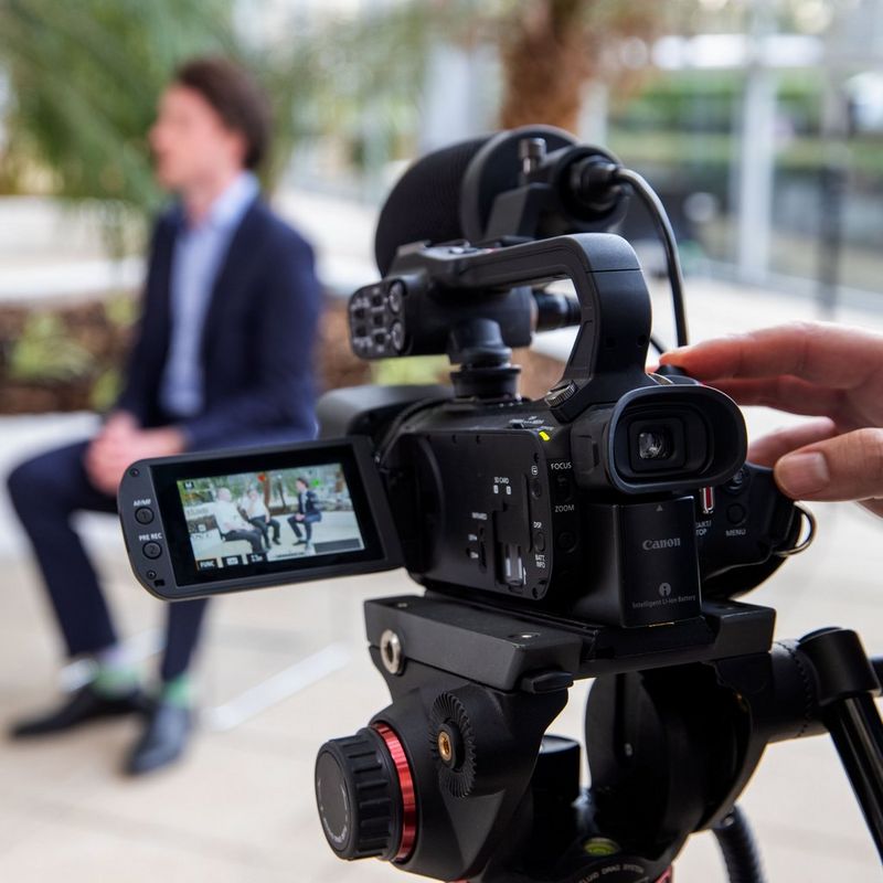 Canon XA45 Camcorder Back Left View with Flipped Screen on Tripod Filming