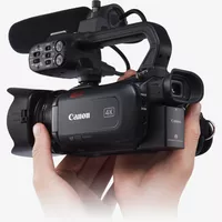Canon XA40 Camcorder Rückansicht von links mit Mikrofon oben und Händen, die den Camcorder tragen