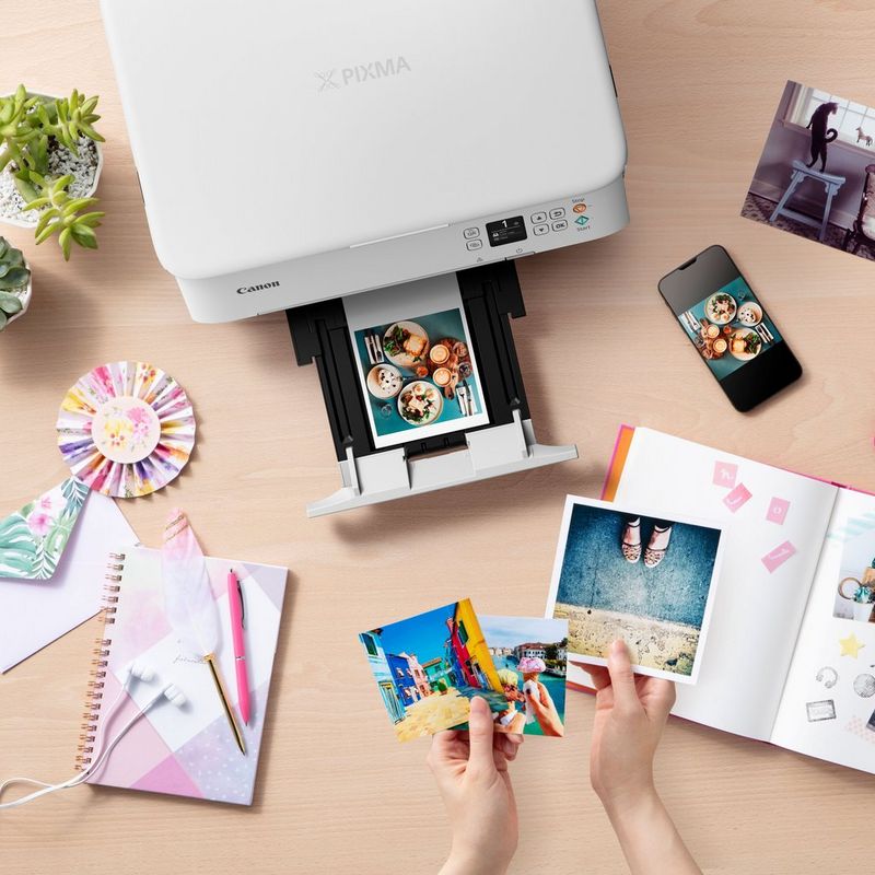 Canon PIXMA TS5351 Tintenstrahl-Multifunktionssystem, Weiß Produkt Ansicht von oben mit einem ausgeklappten Papierfach und einer Person, die die Fotos prüft