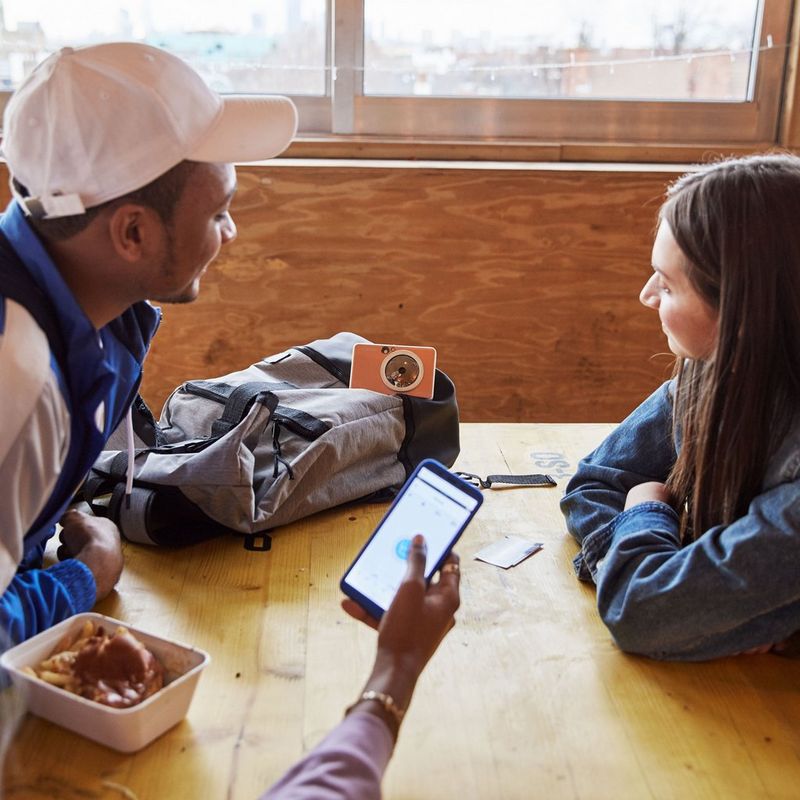 Canon Zoemini S Instant Camera Colour Photo Printer, Rose Gold Printer on Bag with 2 persons looking at it