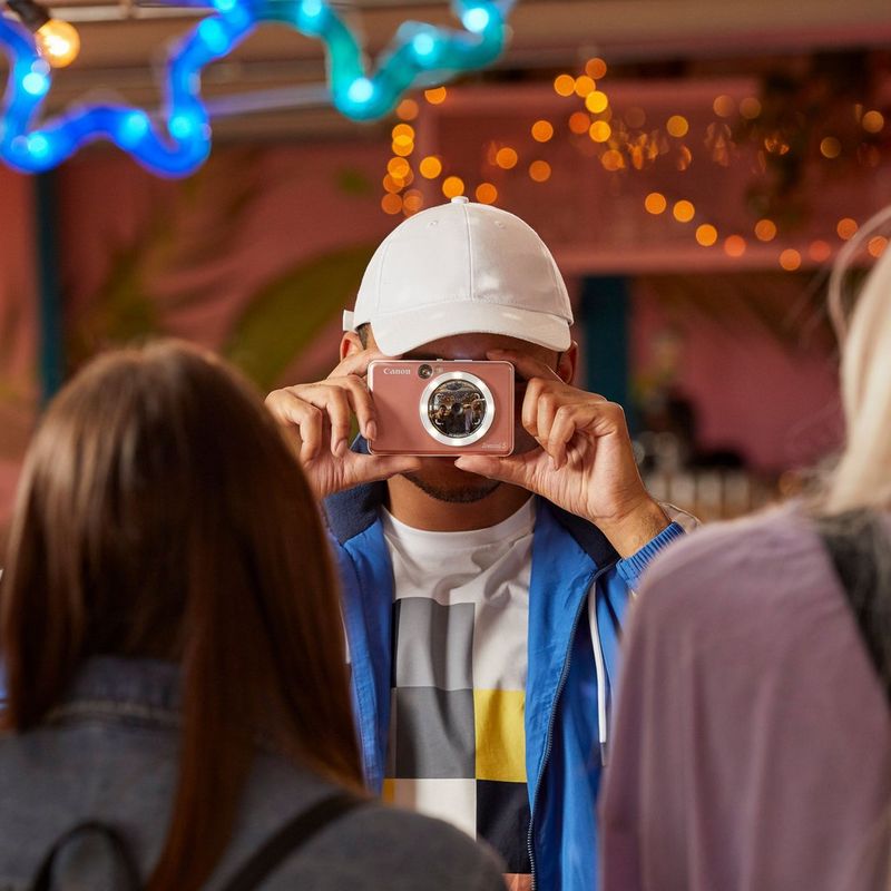 Cámara impresora fotográfica en color instantánea Canon Zoemini S, oro rosa + Diario + Estuche Hombre con una gorra haciendo una foto