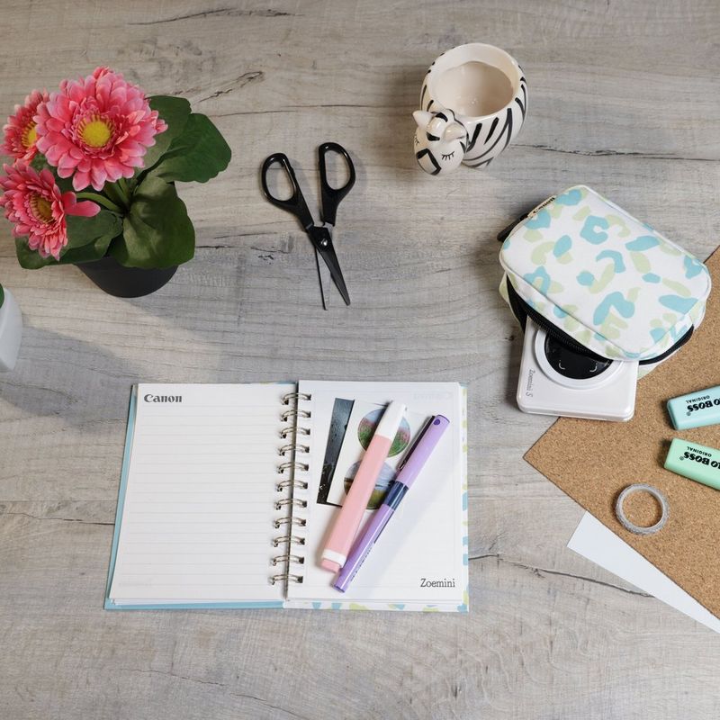 Imprimante photo couleur instantanée Canon Zoemini S, blanc perle + agenda + étui Imprimante installée sur un bureau avec des ciseaux
