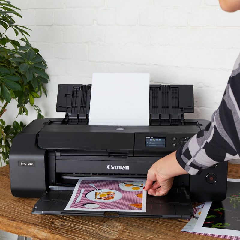 Impresora fotográfica inalámbrica A3 Plus en color PIXMA PRO-200 de Canon Producto Vista frontal de una persona sacando la foto de la bandeja de papel abierta