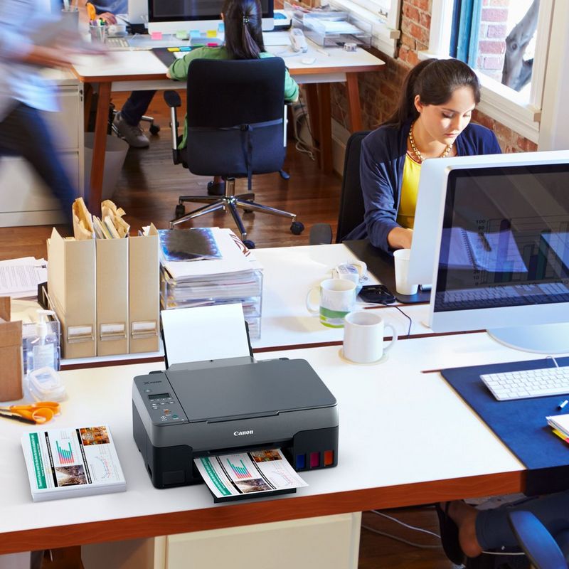 Canon PIXMA G2520 Colour 3-in-1 Refillable MegaTank Printer Kept On A Office Table Beside A Desktop With Paper Tray Out And Paper Support